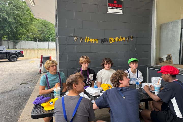Group of young people seated at a table with birthday decorations on a wall.