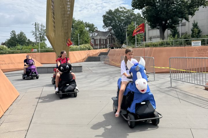 People riding segways on a paved path, trees and buildings in the background.