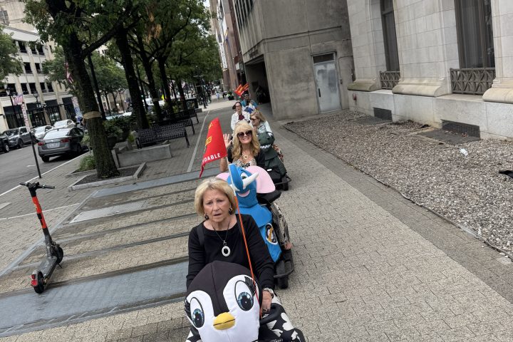 People in costumes walking on a sidewalk, one dressed as a penguin.