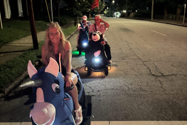 Group riding scooters with animal costumes on a night street.