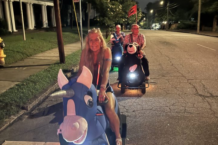 People riding scooters with inflatable cow costumes at night on a street.