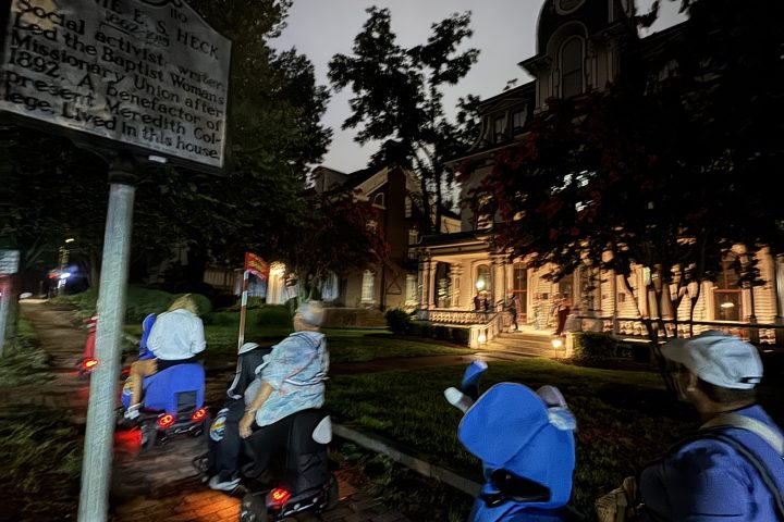 People on scooters near a historic building at dusk.