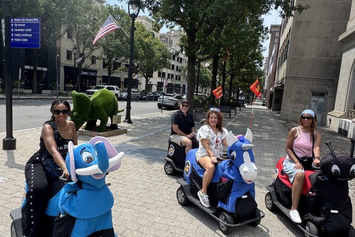 People ride motorized animal scooters on a city sidewalk.