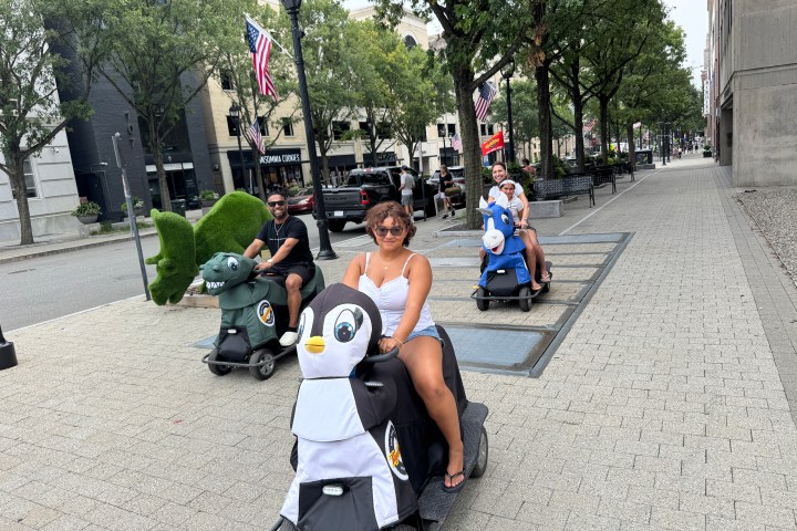 People riding animal-themed scooters on a city sidewalk.