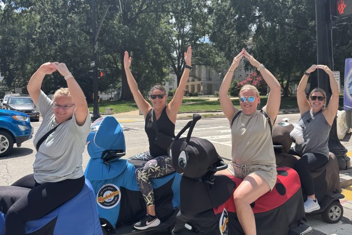 Group of people on scooters posing with arms up at an intersection.