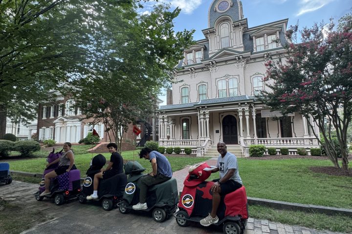 People crouch beside small cars near a historic building.