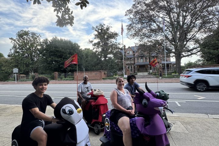 People in motorized animal scooters on a sidewalk under a tree.