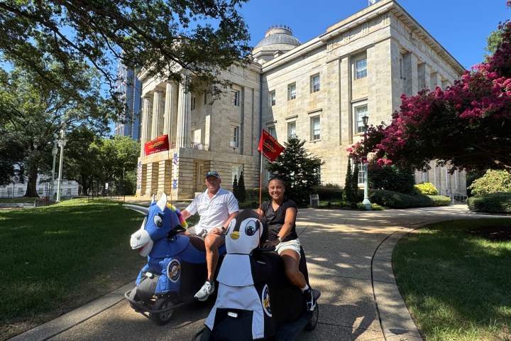 Two people riding animal-shaped scooters near a historic building with columns.
