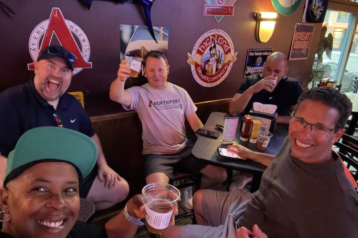 Group of people smiling and enjoying drinks in a bar with wall decorations.