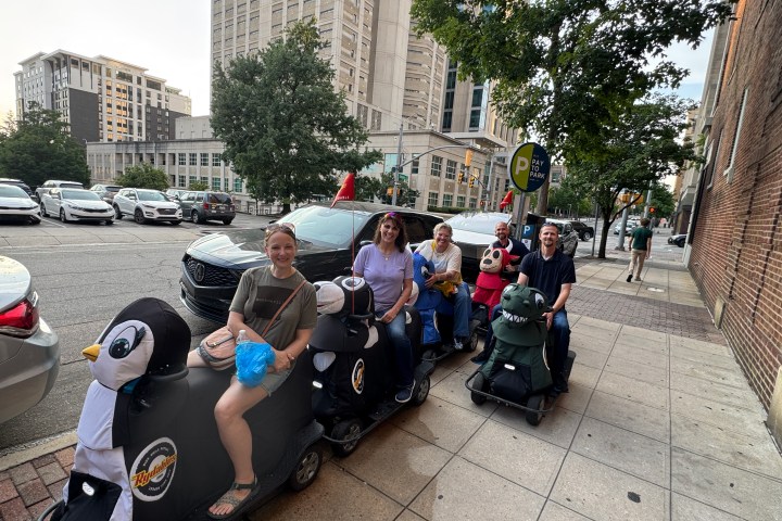People riding animal-shaped scooters on a city sidewalk.