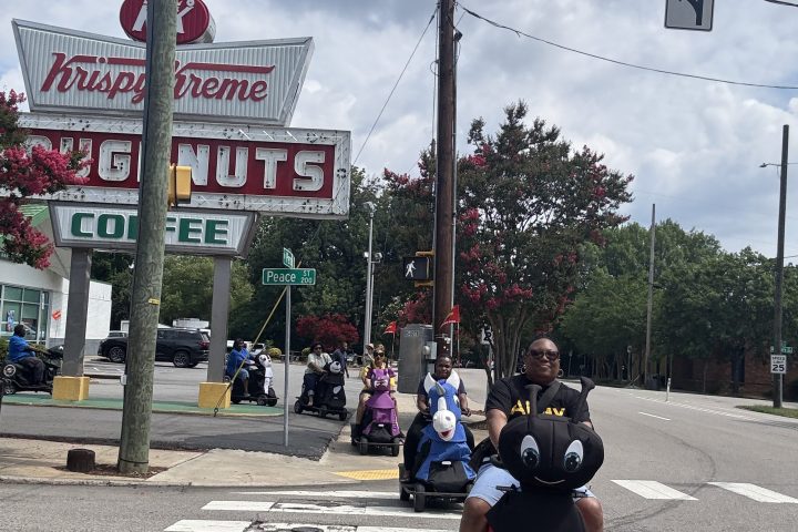 People on scooters near Krispy Kreme with donuts sign in background.