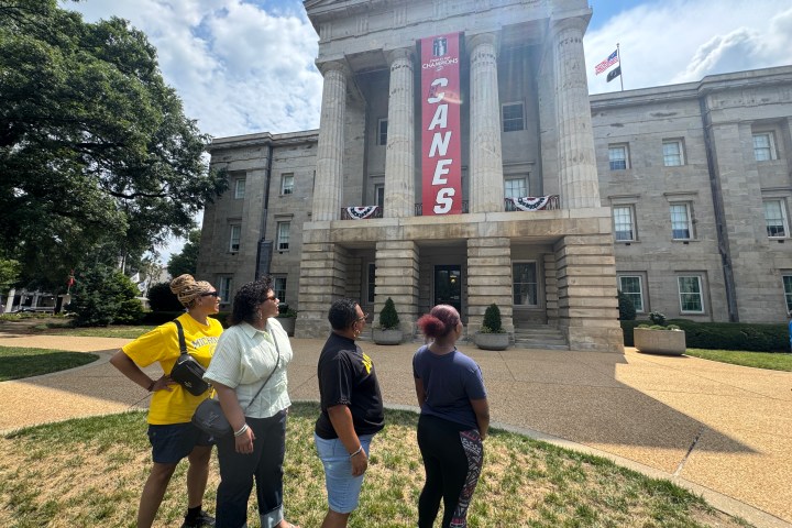 Four people stand outside a large building with columns and a 'CANES' banner.