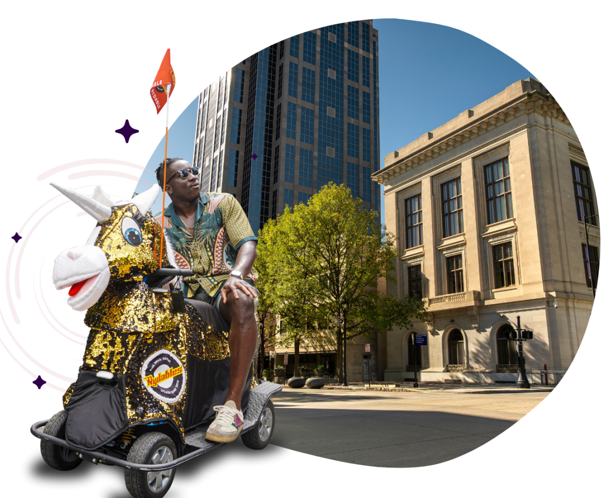 Person on a unicorn-themed scooter with buildings and a tree in the background.