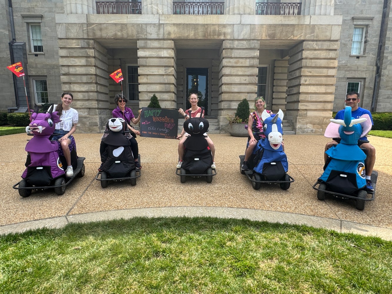Group of people on animal scooters in front of a large building.