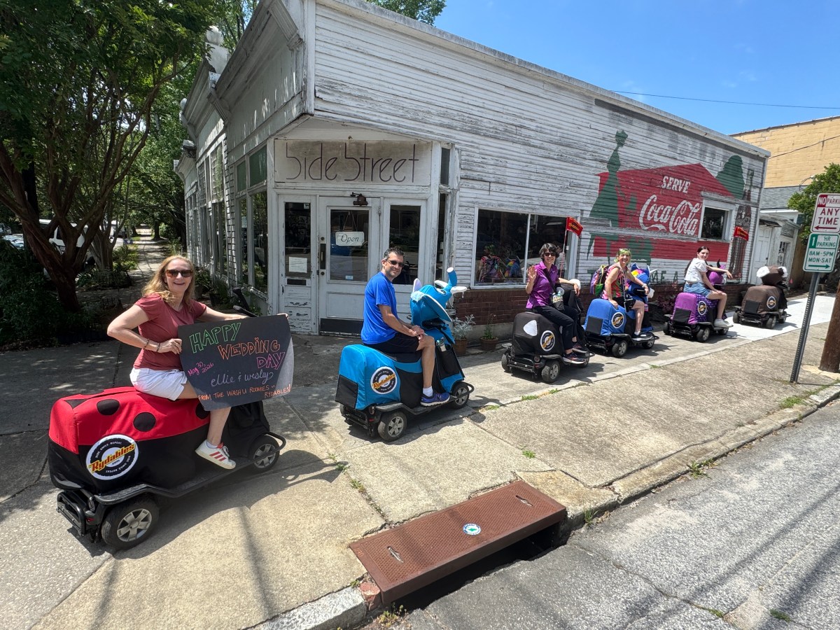 People on scooters in line outside a rustic shop with Coca-Cola mural.