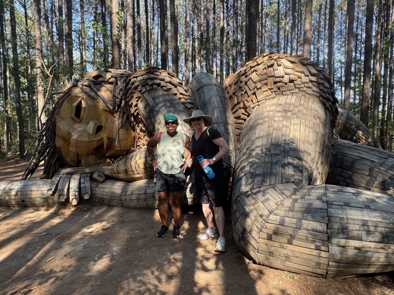 Two people sit on a large wood sculpture in a forest.