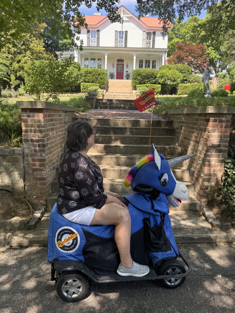 Person on mobility scooter with unicorn cover, outside a house with brick steps.
