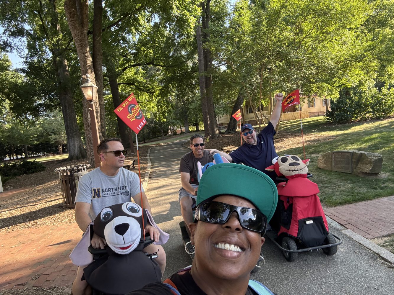 Group of people outdoors with a wagon and flags, smiling and enjoying a sunny day.